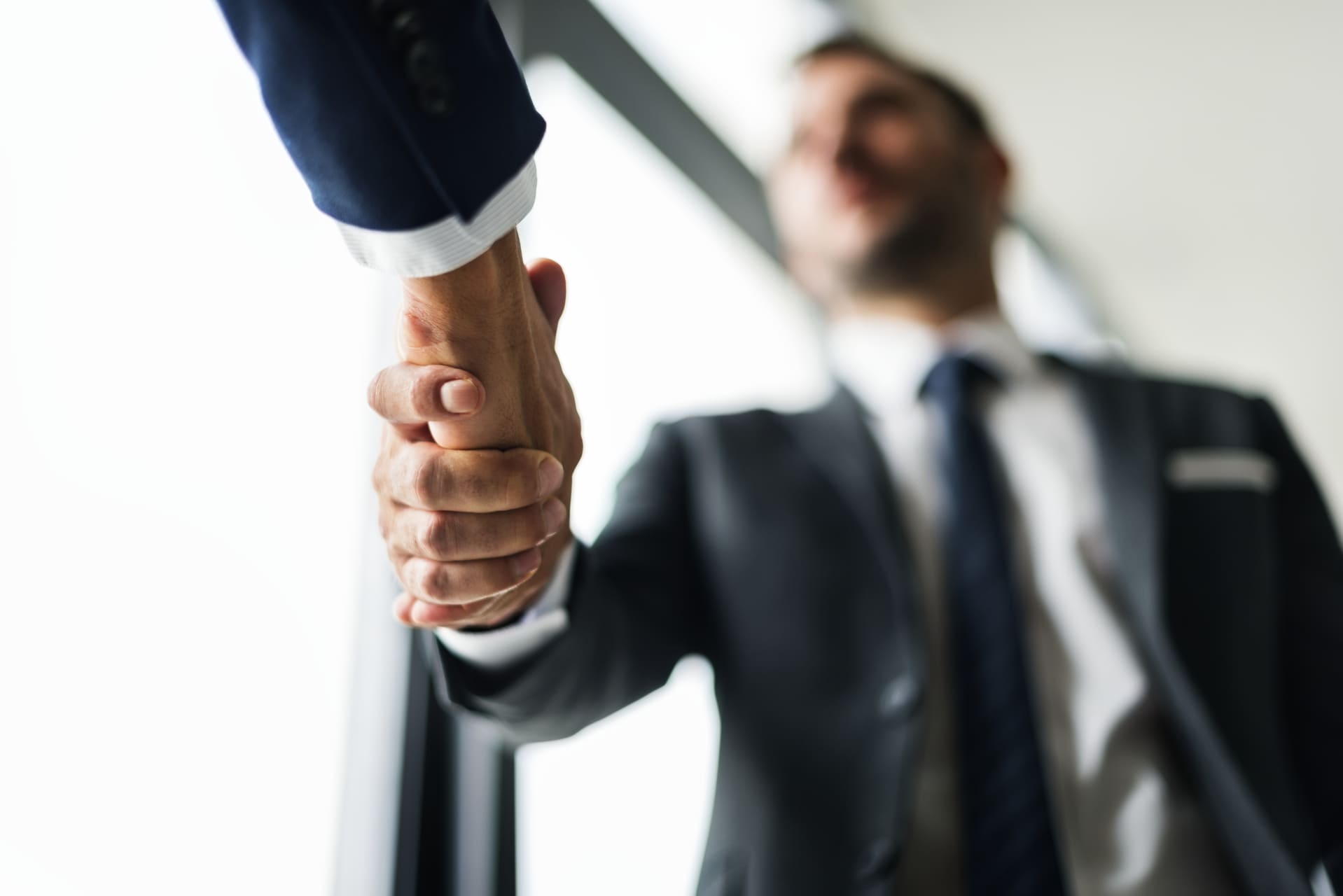 Un primer plano de un apretón de manos entre dos hombres de negocios, con énfasis en la conexión y acuerdo, reflejando la confianza y colaboración en el entorno profesional.